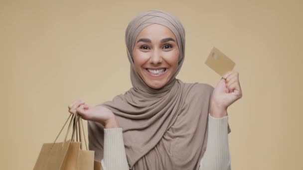 Junge glückliche Frau aus dem Nahen Osten trägt traditionellen Hijab mit Kreditkarte und bettelt lächelnd in die Kamera — Stockvideo