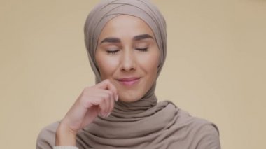 Düşünceli genç bir ortadoğulu kadının portresi tesettür takan ya da planlayan, bej arka planda poz veren