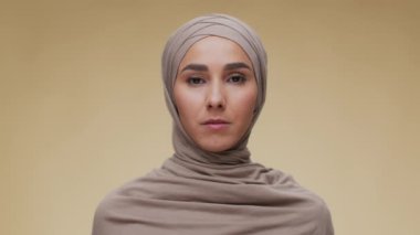 Geleneksel başörtüsü takmış, kameraya bakan ciddi Müslüman bir kadının stüdyo portresi.