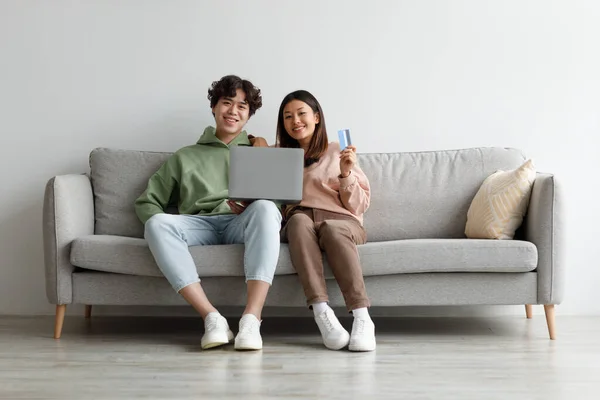 Online-Shopping. Asiatisches Paar sitzt zu Hause auf der Couch, nutzt Laptop und Kreditkarte, kauft Waren im Webshop — Stockfoto