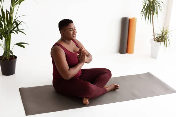 Relajada mujer afroamericana con sobrepeso meditando en estudio de yoga —  Fotos de Stock