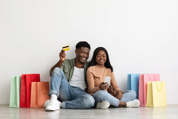 Emocionální afroameričtí pár shopaholics pomocí smartphone a kreditní karty — Stock fotografie