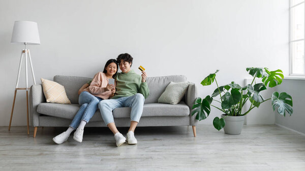 Покупки онлайн. Молодая азиатская пара, совершающая покупки на мобильном телефоне, держащая кредитные карты, используя услуги веб-банкинга