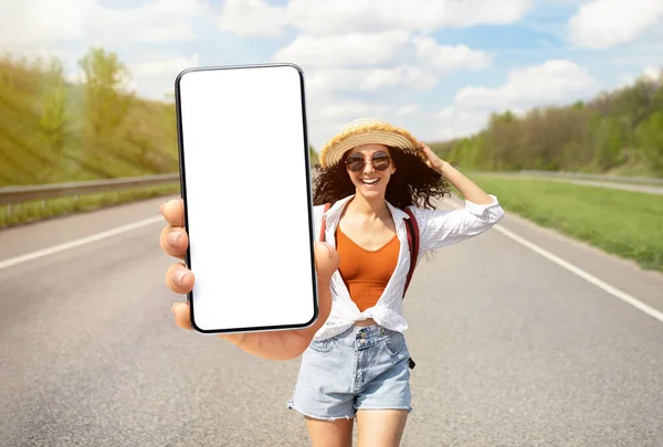 Ενθουσιασμένη νεαρή ταξιδιώτης γυναίκα στέκεται στην εθνική οδό και δείχνει μεγάλο κενό Smartphone — Φωτογραφία Αρχείου