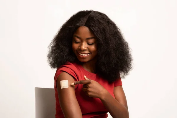 รูปภาพของการฉีดวัคซีนแอฟริกันอเมริกันหญิงชี้ที่ผ้าพันแผลกาวบนแขน — ภาพถ่ายสต็อก