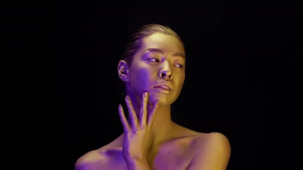 Mujer con piel dorada posando en luz de neón, fondo negro — Vídeos de Stock