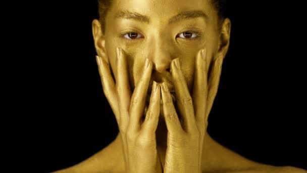 Kobieta ze złotą skórą dotykająca twarzy na czarnym tle — Wideo stockowe
