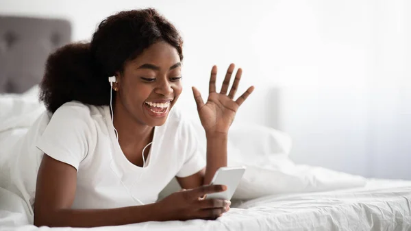 Alegre negro mujer tendida en la cama, teniendo video chat —  Fotos de Stock