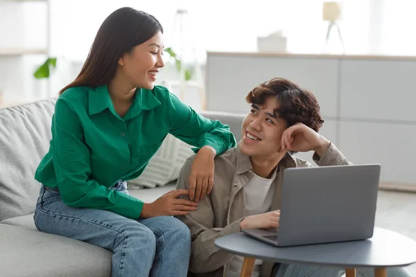 积极的千年期亚洲夫妇使用笔记本电脑，互相微笑，在家里一起浏览互联网 — 图库照片