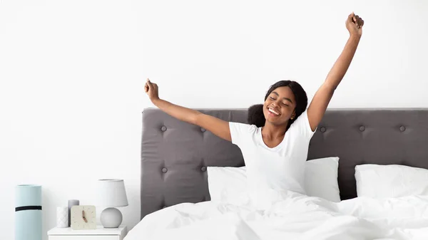 İyi dinlenmiş siyah kadın mutlu bir sabah geçiriyor, yatakta geriniyor. — Stok fotoğraf