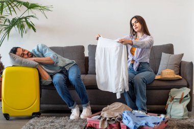 Tatil için hazırlık. Kocası oturma odasındaki kanepede yatarken kadınlar bavullarını topluyor.