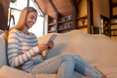 Evde akıllı telefon kullanan gülümseyen bir kadının portresi