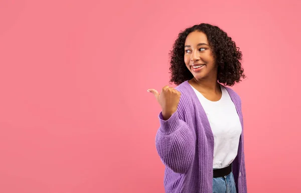 Feliz joven mujer negra señalando a un lado en el espacio libre en el fondo del estudio rosa — Foto de Stock