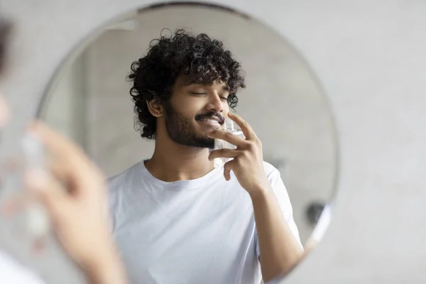 Satisfied indian man smelling perfume, doing morning beauty routine, enjoying pleasant odor, standing in bathroom — Stock Photo, Image