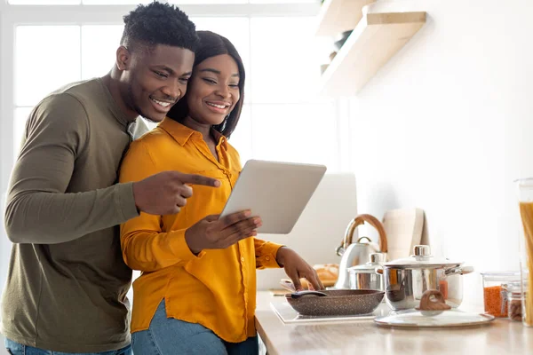 Ευτυχισμένο μαύρο ζευγάρι χρησιμοποιώντας ψηφιακή ταμπλέτα, ενώ το μαγείρεμα των τροφίμων μαζί στην κουζίνα — Φωτογραφία Αρχείου