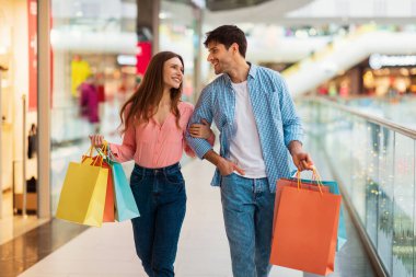 Alışveriş yapan çift, alışveriş torbalarını modern hipermarkette gezdiriyor.