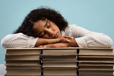 Yorgun Afrikalı Amerikalı kız öğrenci kitapların üzerinde uyuyor, sınavlara hazırlanırken yoruluyor.