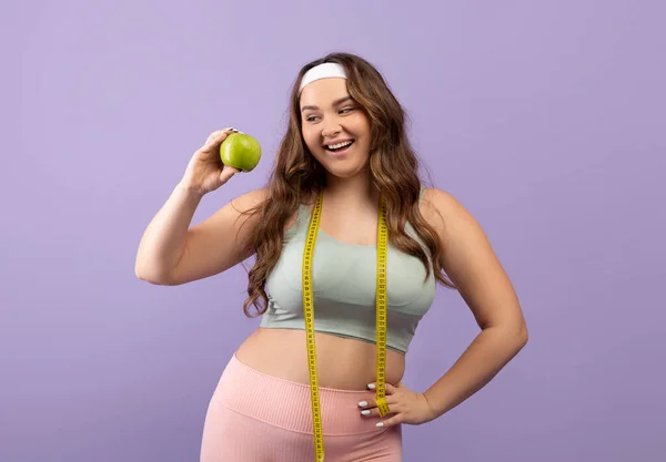 Glad kaukasiska plus storlek ung kvinna i sportkläder med måttband visa grönt äpple — Stockfoto