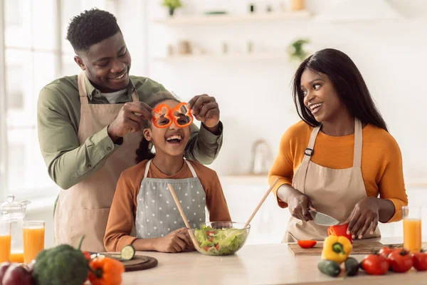 Familia africana haciendo ensalada divirtiéndose con verduras en la cocina — Foto de Stock