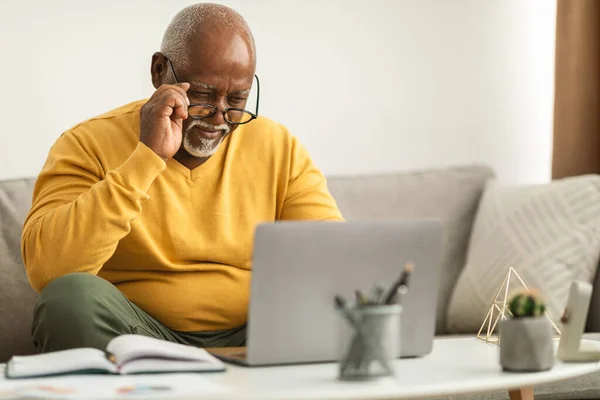 アフリカ系のシニア男性が眼鏡をかけてノートパソコンを使って目を細める室内 — ストック写真