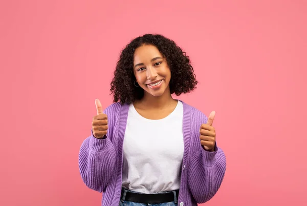 Hermosa joven mujer negra en ropa casual que muestra el gesto de pulgar hacia arriba, expresando positividad en el fondo del estudio rosa — Foto de Stock