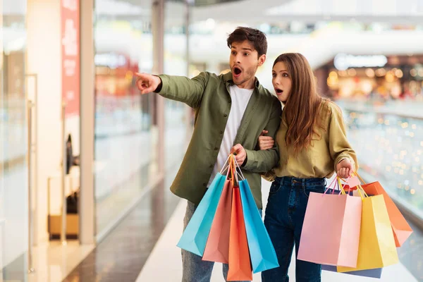 Casal incrível fazendo compras apontando o dedo para fora no shopping — Fotografia de Stock