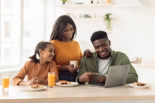 Familia afroamericana feliz almorzando usando el ordenador portátil en la cocina — Foto de Stock
