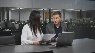 İş görüşmeleri konsepti. Genç adam ve kadın ortaklar sözleşme detaylarını tartışıyor, ofiste birlikte oturuyorlar.