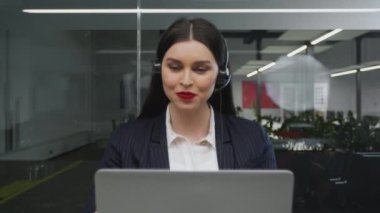 Genç bayan müşteri destek operatörü ya da kulaklık takan satış temsilcisi bilgisayardan müşteriyle görüntülü konuşma yapıyor.