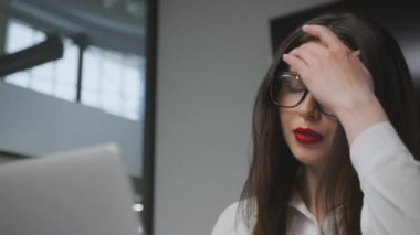 Aşırı çalışma konsepti. Ofiste dizüstü bilgisayarda yazan gözlüklü genç ve yorgun bir iş kadını.