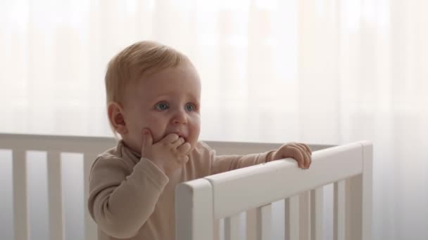 Kinderziektes bij baby 's. Schattig kind staand in bed en kauwende vingers — Stockvideo