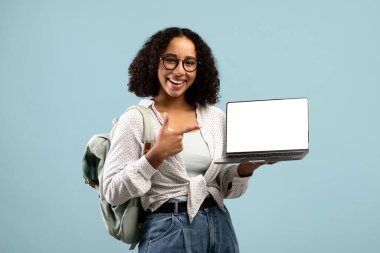 Çevrimiçi eğitim sitesi. Sırt çantalı gülümseyen siyah kız öğrenci boş beyaz ekranlı dizüstü bilgisayarını gösteriyor.