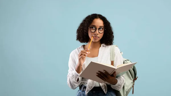 Zamyšlená černá studentka čtení knihy, přemýšlení nad úkolem na modrém pozadí studia, prapor s volným místem — Stock fotografie