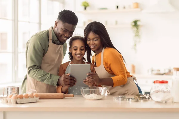 Hornear familia negra usando la tableta digital que cocina la torta en la cocina — Foto de Stock