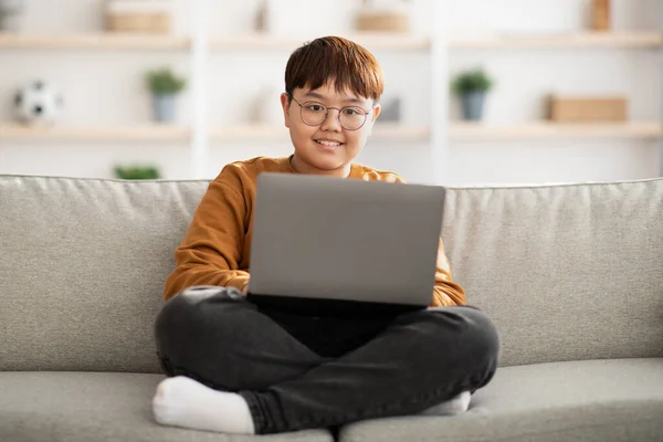 Felice bambino cinese seduto sul divano con computer portatile a casa — Foto Stock