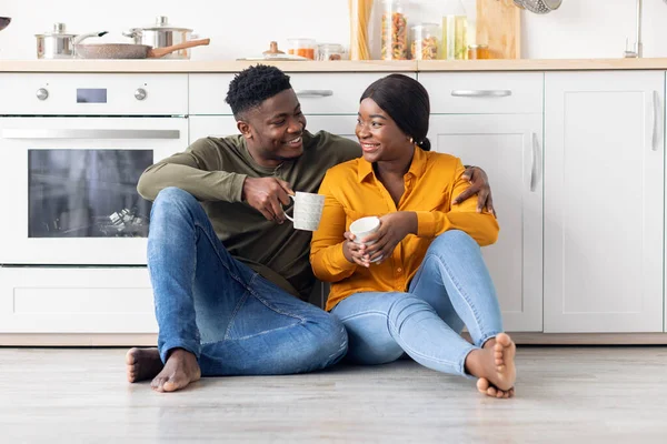 Romantique noir couple millénaire relaxant avec café dans la cuisine, assis sur le sol — Photo