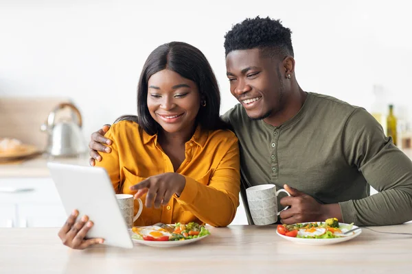 Glückliche schwarze Ehepartner frühstücken gemeinsam und verwenden digitale Tablets in der Küche — Stockfoto