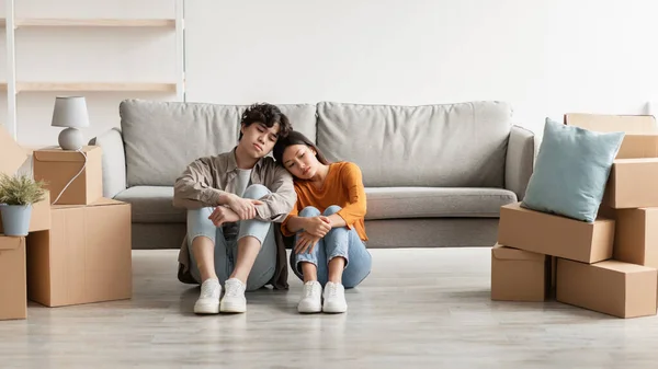 Расстроенная молодая азиатская пара, сидящая на полу среди картонных коробок, чувствующая себя измученной и грустной в день переезда, пустое пространство — стоковое фото