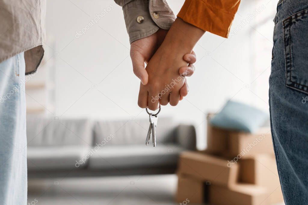 Closeup of young couple holding hands and new house key, moving in together. Mortgage, real estate concept