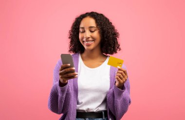 Yeni online alışveriş uygulaması. Akıllı telefon ve kredi kartı kullanan, internet mağazasından mal alan çekici siyahi kadın.