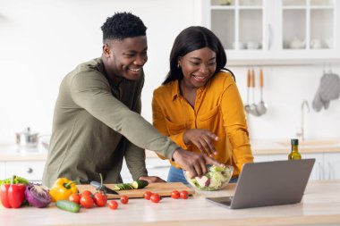 Neşeli Siyah Çift Mutfakta Sağlıklı Yemek Pişirirken Dizüstü bilgisayar kullanıyor