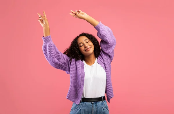 Portarit of excited young black lady dancing, celebrating success or victory on pink studio background