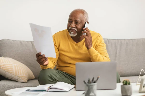 Старший афроамериканский бизнесмен разговаривает по телефону, держа бумагу в помещении — стоковое фото