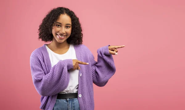 Alegre joven hembra negra apuntando al espacio libre sobre fondo de estudio rosa, panorama — Foto de Stock