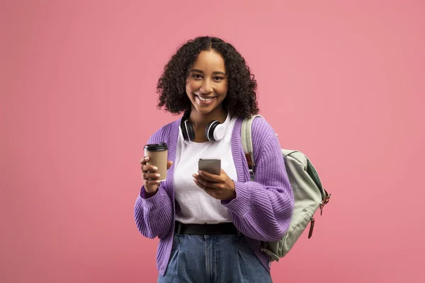 Boldog fekete nő hátizsák és fejhallgató ivás elvitelre kávé, mobiltelefon, üzenetküldés online — Stock Fotó