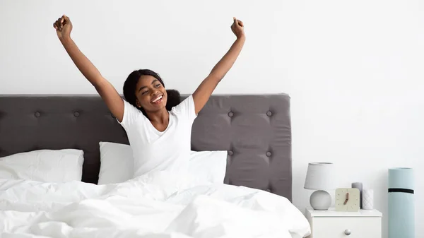 Mujer negra alegre disfrutando de la mañana feliz, estirándose en la cama —  Fotos de Stock
