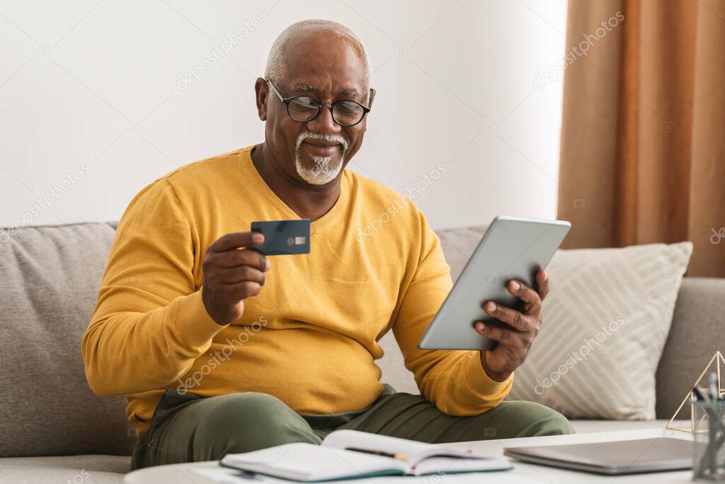 Senior African Man Shopping Using Credit Card And Tablet Indoor