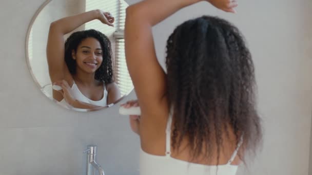 衛生的な化粧品。若いですアフリカ系アメリカ人女性適用スティック消臭剤で彼女の脇の下,見てミラーでバスルーム — ストック動画