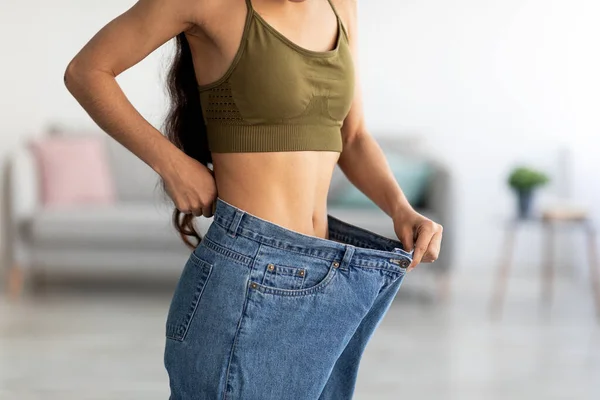 Successful weight loss diet. Closeup of young Indian lady in big jeans demonstrating results of her slimming program — Stock Photo, Image