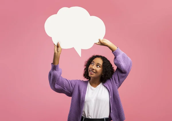 Позитивна чорна жінка тримає порожню бульбашку мови над головою на рожевому фоні студії, макет для дизайну реклами — стокове фото